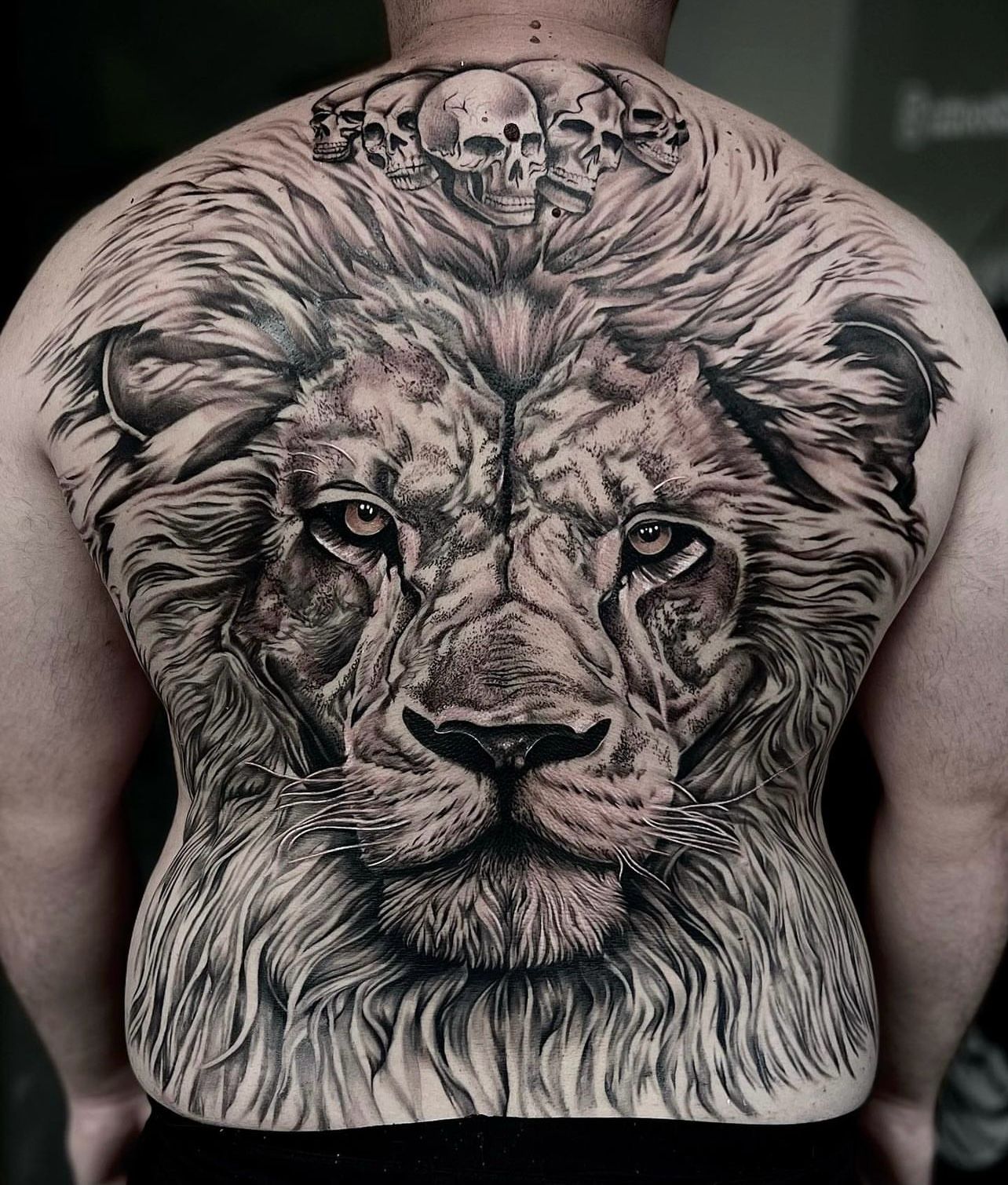 Back tattoo featuring a detailed lion face with skulls