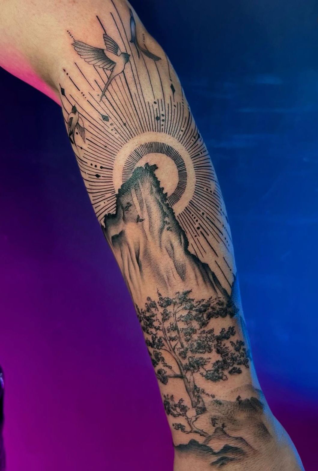 Nature scene forearm tattoo with mountain and sun rays